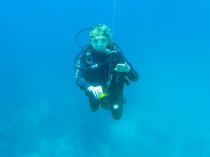 Joyce Lindsay practices an emergency ascent using a Surface Marker Buoy (SMB) in the Galápagos Islands, where powerful currents and unpredictable surface conditions make SMB deployment an essential safety skill for divers. In these dynamic conditions, SMBs are required to ensure divers can surface safely and be seen by support vessels. Joyce Lindsay on a dive boat preparing to deploy a Surface Marker Buoy during an emergency ascent drill in the strong‑current waters of the Galápagos Islands.